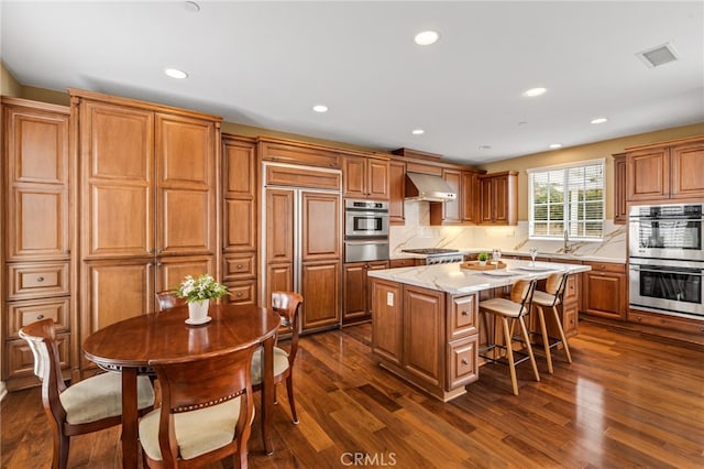 kitchen with visible vents, dark wood-type flooring, a center island, stainless steel appliances, and wall chimney range hood