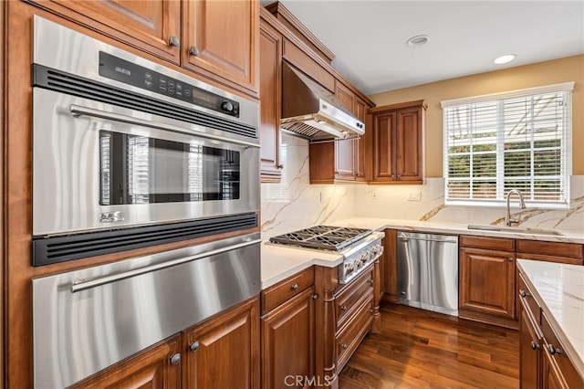 kitchen featuring tasteful backsplash, dark wood finished floors, appliances with stainless steel finishes, under cabinet range hood, and a sink