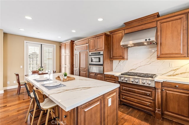 kitchen with paneled built in refrigerator, wall chimney exhaust hood, brown cabinetry, and stainless steel gas stovetop