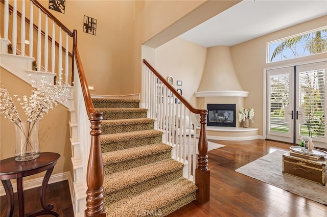 staircase featuring a large fireplace, french doors, baseboards, and wood finished floors