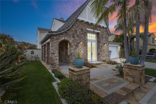 view of front of house with a garage, concrete driveway, french doors, stone siding, and a front yard