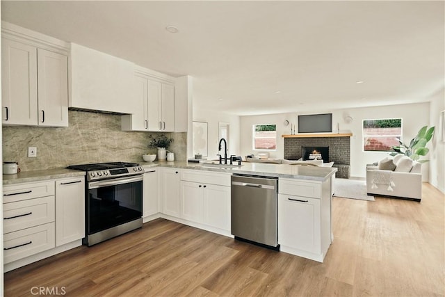 kitchen with a peninsula, stainless steel appliances, light wood-type flooring, white cabinetry, and a sink