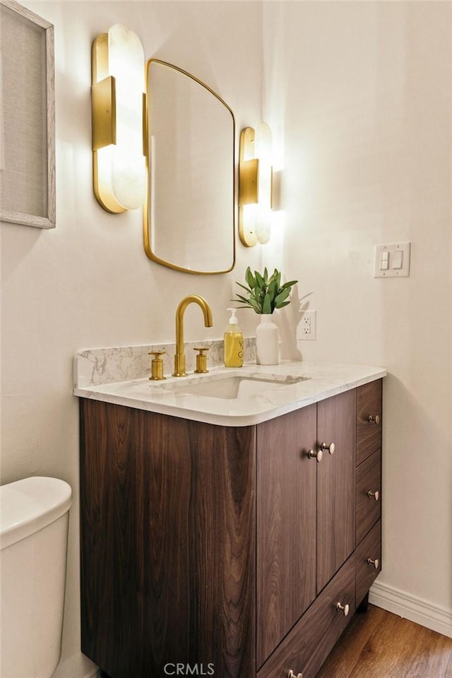 half bathroom with baseboards, vanity, toilet, and wood finished floors