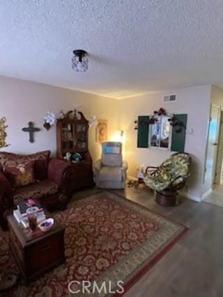 living area with visible vents, a textured ceiling, and wood finished floors