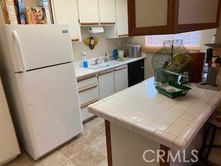 kitchen with tile counters, freestanding refrigerator, and white cabinets