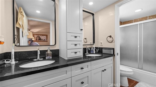 bathroom featuring enclosed tub / shower combo, a sink, toilet, and double vanity