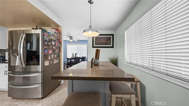 kitchen with stainless steel refrigerator with ice dispenser, a breakfast bar area, light tile patterned floors, hanging light fixtures, and white cabinetry