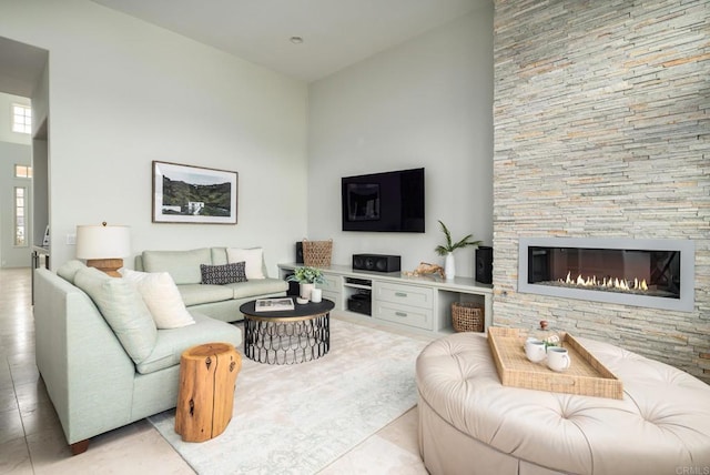 living room with light tile patterned floors, a high ceiling, and a stone fireplace