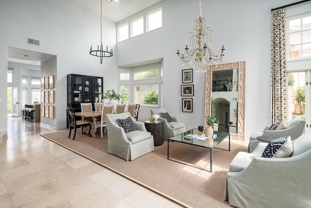 living room featuring a chandelier, visible vents, a healthy amount of sunlight, and a towering ceiling