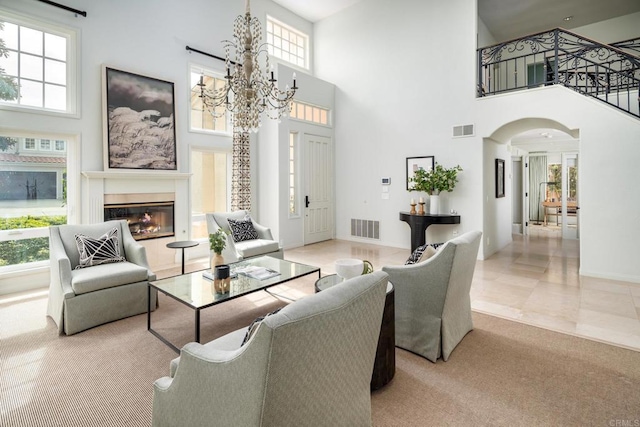carpeted living room featuring a glass covered fireplace, a notable chandelier, arched walkways, and visible vents