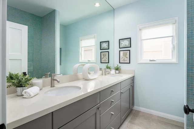 full bath with double vanity, tile patterned flooring, baseboards, and a sink