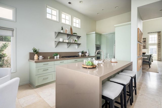 kitchen featuring visible vents, a breakfast bar, open shelves, stainless steel appliances, and green cabinets