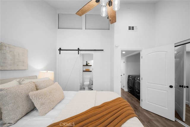 bedroom with a barn door, a high ceiling, wood finished floors, visible vents, and washer and clothes dryer