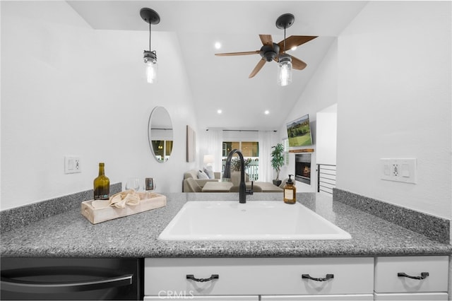 kitchen featuring ceiling fan, open floor plan, a lit fireplace, vaulted ceiling, and a sink