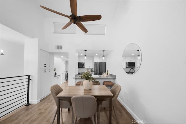 dining area with light wood-type flooring, baseboards, a high ceiling, and visible vents