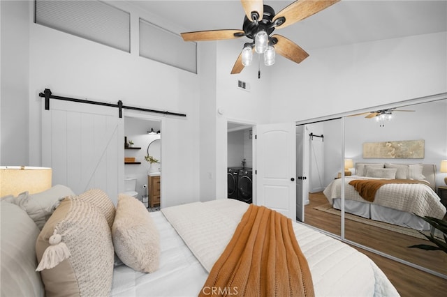 bedroom featuring a barn door, visible vents, wood finished floors, and independent washer and dryer