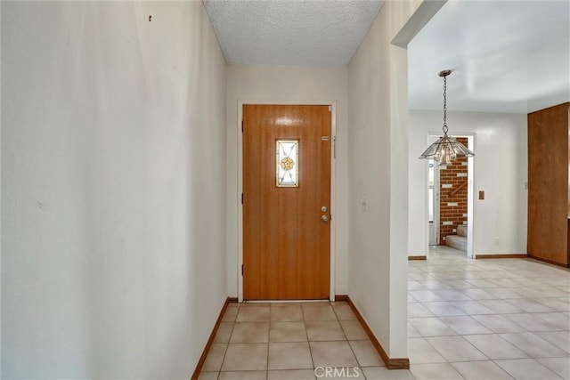 doorway with light tile patterned floors, a textured ceiling, and baseboards