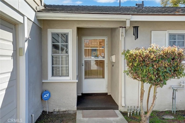 doorway to property featuring stucco siding and a shingled roof