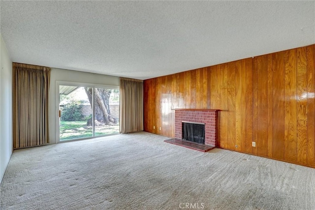 unfurnished living room with a textured ceiling, a brick fireplace, wood walls, and carpet floors