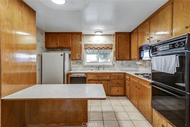 kitchen featuring a sink, black appliances, brown cabinetry, and light countertops