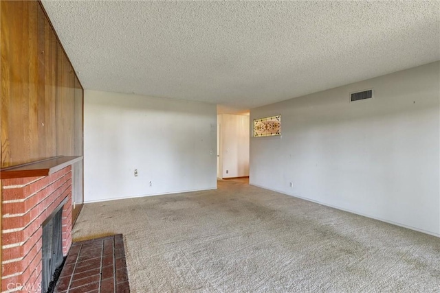 unfurnished living room featuring visible vents, dark carpet, a textured ceiling, and a fireplace