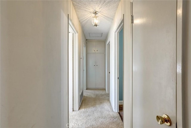 corridor featuring attic access, carpet, and a textured ceiling