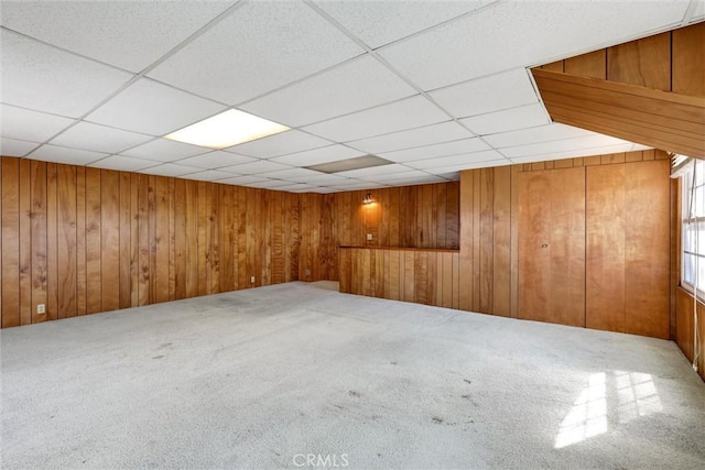 finished basement featuring a paneled ceiling, wood walls, and carpet flooring