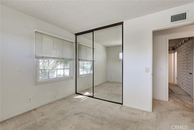 unfurnished bedroom with carpet flooring, visible vents, a closet, and a textured ceiling