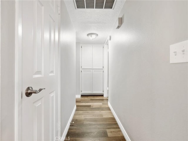 hall with visible vents, a textured ceiling, baseboards, and wood finished floors