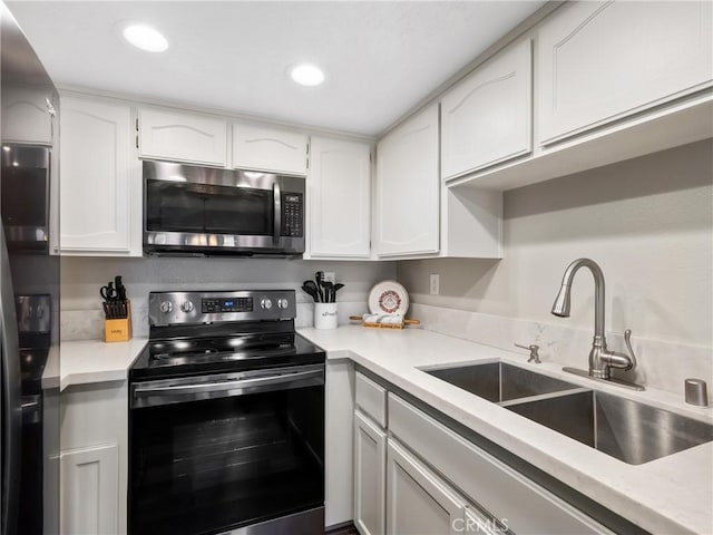 kitchen featuring electric stove, stainless steel microwave, light countertops, white cabinetry, and a sink