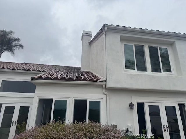 view of side of property with stucco siding, a tiled roof, a chimney, and french doors