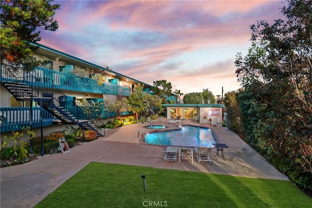 community pool with a yard, a patio, a hot tub, and stairs