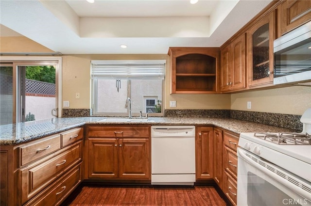 kitchen with white appliances, stone counters, brown cabinetry, and a sink