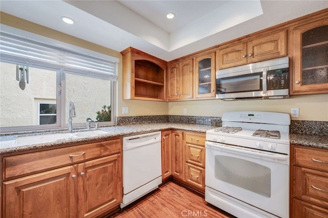 kitchen featuring a tray ceiling, white appliances, brown cabinetry, and a sink