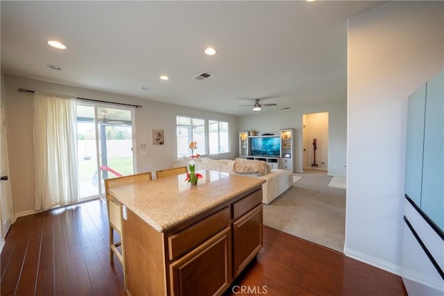 kitchen with dark wood-type flooring, brown cabinetry, a kitchen island, and visible vents