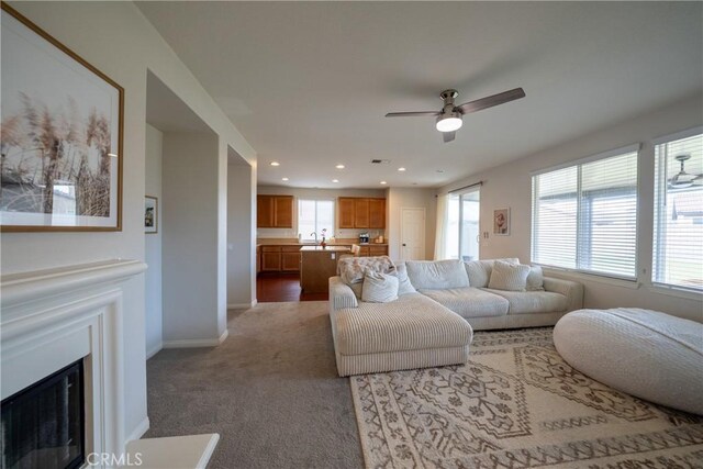 carpeted living room featuring baseboards, ceiling fan, a fireplace, a sink, and recessed lighting