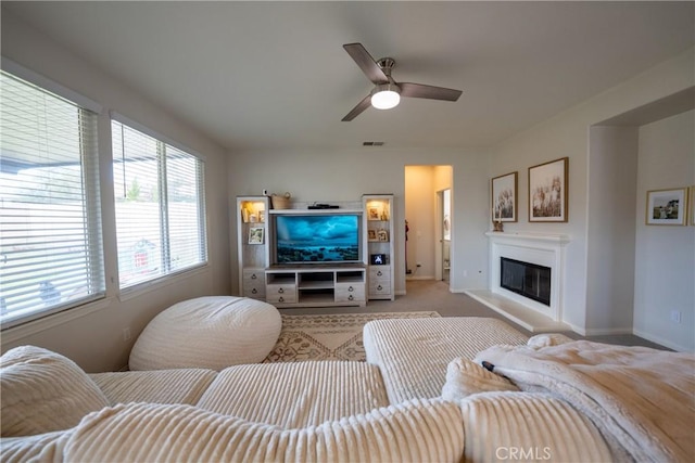 living room featuring baseboards, visible vents, a ceiling fan, a glass covered fireplace, and light colored carpet