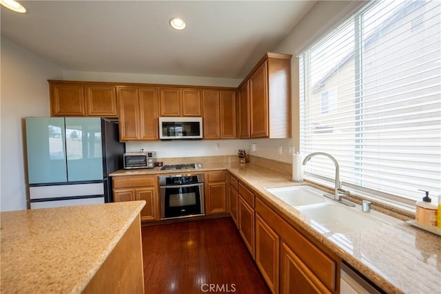 kitchen with dark wood-style floors, stainless steel appliances, brown cabinetry, and a sink