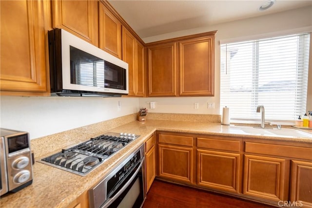 kitchen with brown cabinetry, appliances with stainless steel finishes, light countertops, and a sink