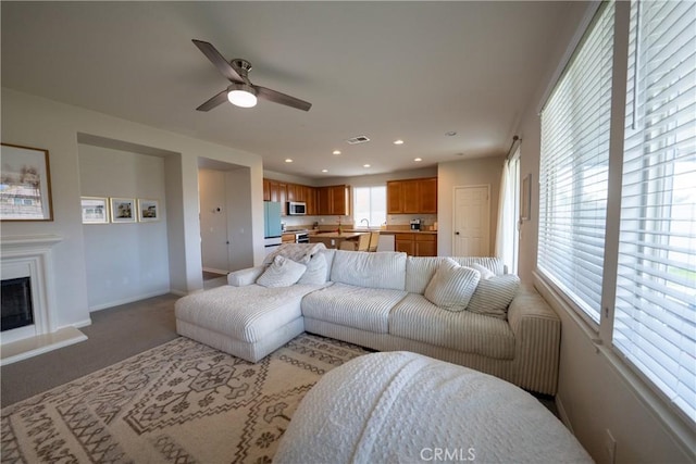 living area with light carpet, baseboards, visible vents, a fireplace with raised hearth, and recessed lighting