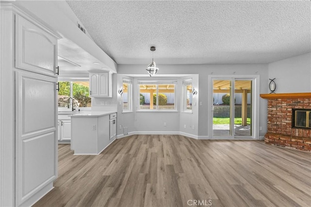 unfurnished living room featuring a sink, a textured ceiling, light wood-style floors, baseboards, and a brick fireplace