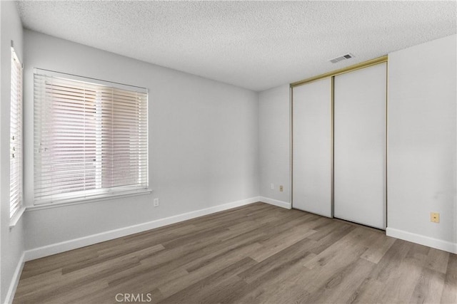 unfurnished bedroom featuring visible vents, baseboards, wood finished floors, a closet, and a textured ceiling