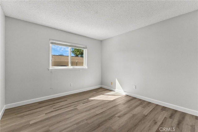 unfurnished room with a textured ceiling, baseboards, and wood finished floors