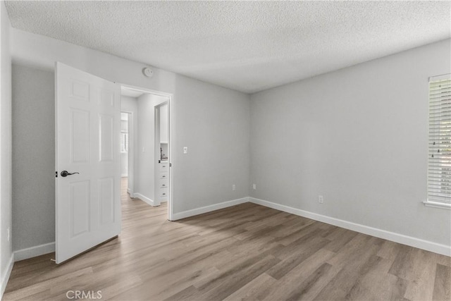 empty room featuring light wood-style flooring, baseboards, and a textured ceiling