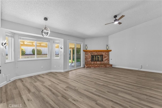 unfurnished living room with a brick fireplace, a textured ceiling, baseboards, and wood finished floors