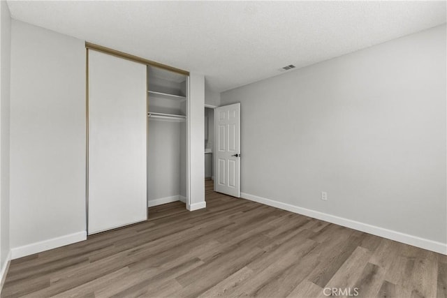 unfurnished bedroom featuring a closet, visible vents, baseboards, and wood finished floors