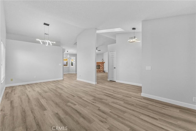 unfurnished living room with a brick fireplace, baseboards, light wood-type flooring, and lofted ceiling