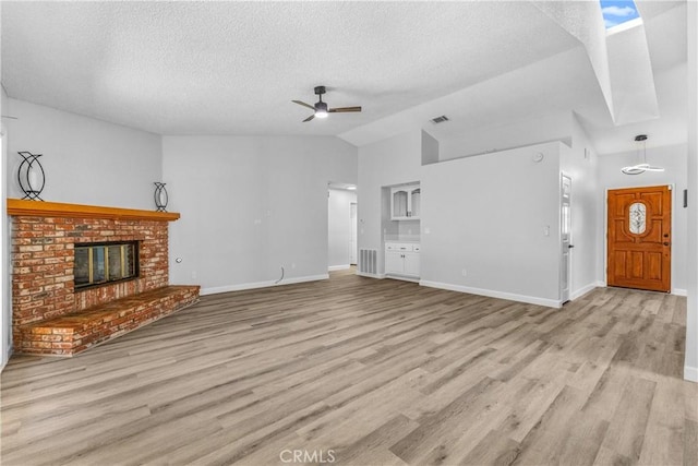 unfurnished living room featuring a brick fireplace, ceiling fan, lofted ceiling, wood finished floors, and a textured ceiling