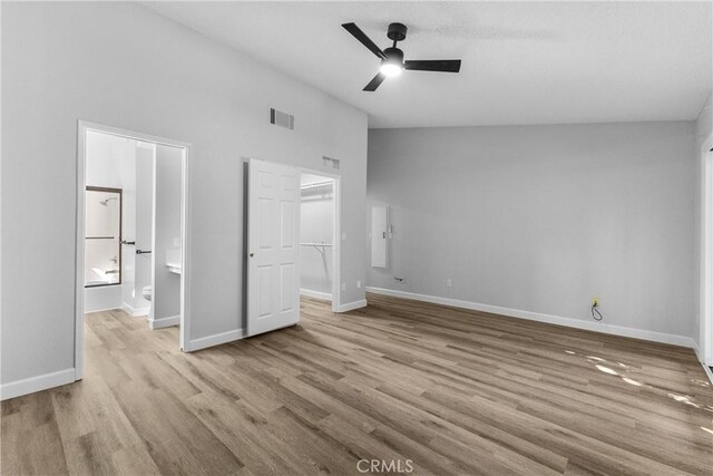 unfurnished bedroom featuring a spacious closet, visible vents, baseboards, lofted ceiling, and wood finished floors