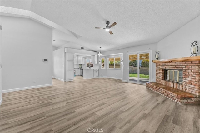 unfurnished living room with lofted ceiling, a brick fireplace, light wood-type flooring, and a textured ceiling